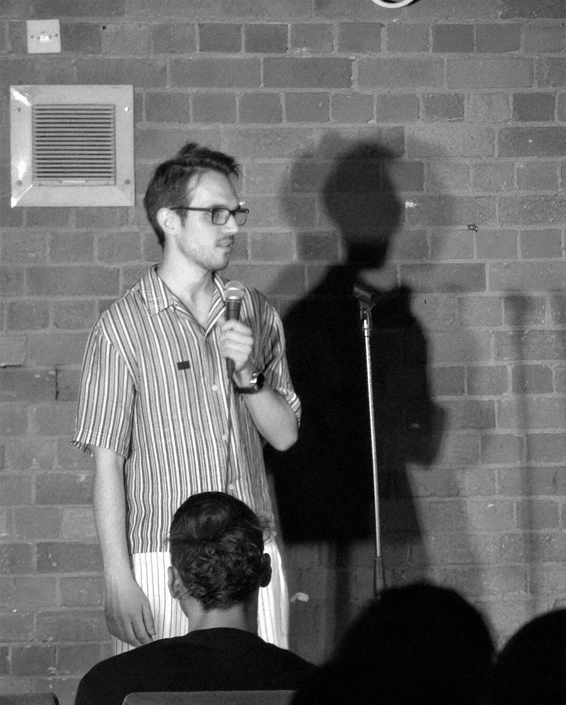 Dylan on stage with a microphone, his shadow on the brick wall behind him